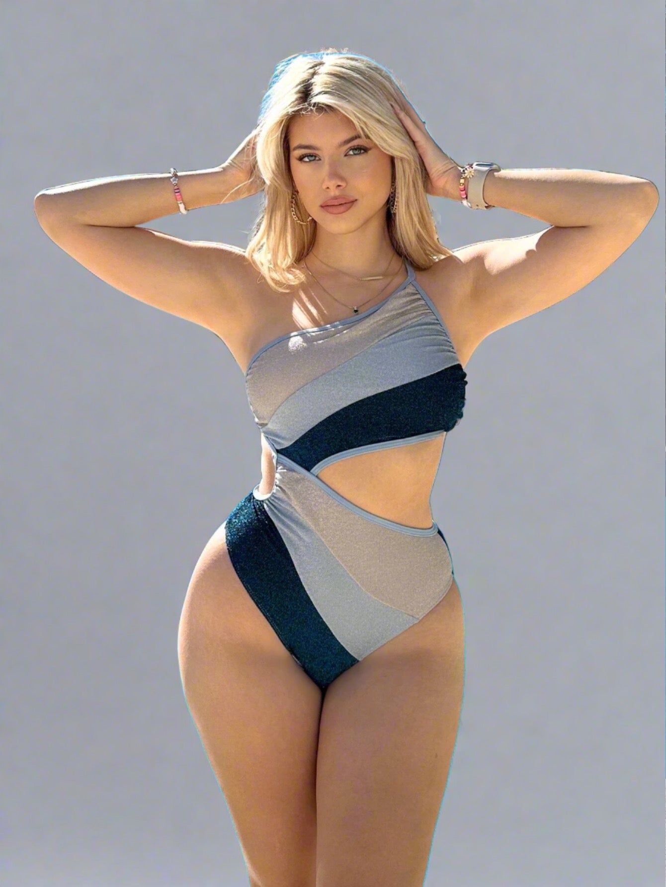 Woman wearing an Asymmetric Cut-Out One-Piece Swimsuit with a color-block pattern in shades of blue and gray, featuring a one-shoulder strap and bold cut-out details.