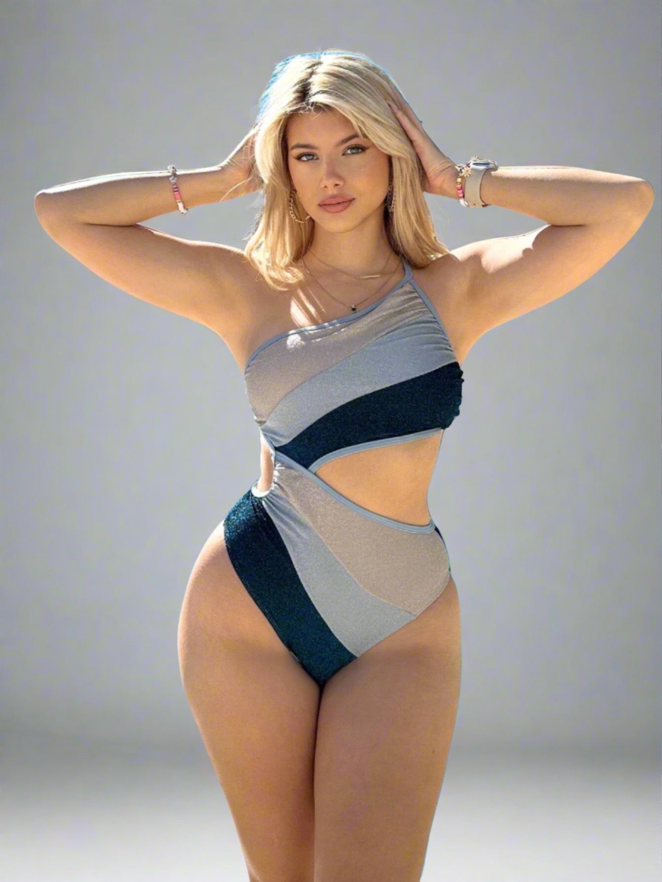 Woman wearing an Asymmetric Cut-Out One-Piece Swimsuit with a color-block pattern in shades of blue and gray, featuring a one-shoulder strap and bold cut-out details.