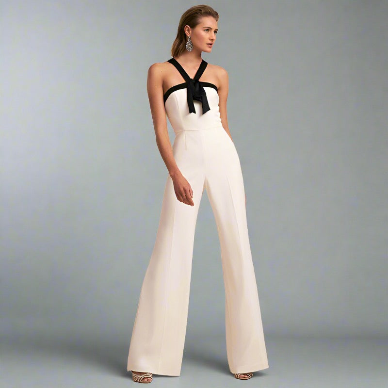 Woman wearing a white halter jumpsuit with a black bow detail and wide-leg design, ideal for elegant travel occasions.