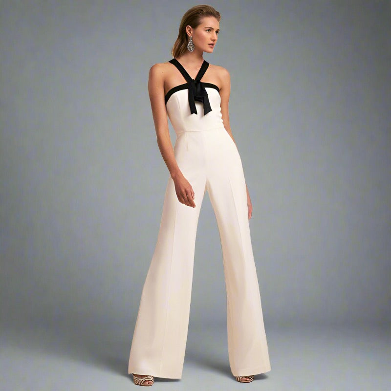 Woman wearing a white halter jumpsuit with a black bow detail and wide-leg design, ideal for elegant travel occasions.