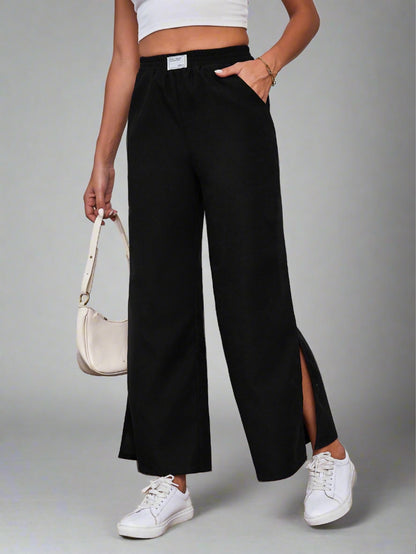 Woman wearing black wide-leg lounge pants with an elastic waistband and side slits, paired with a white crop top and sneakers.