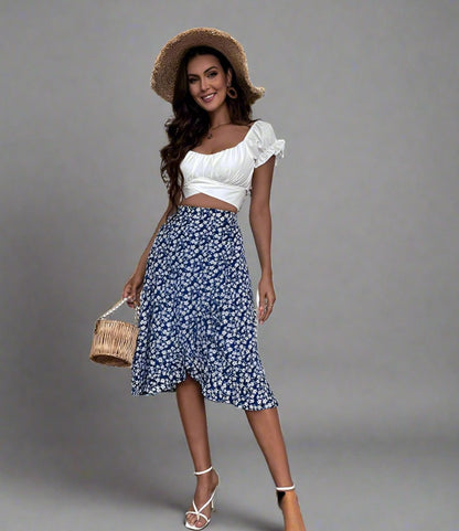 Woman wearing a blue midi skirt with a white floral print, paired with a white crop top and white strappy heels