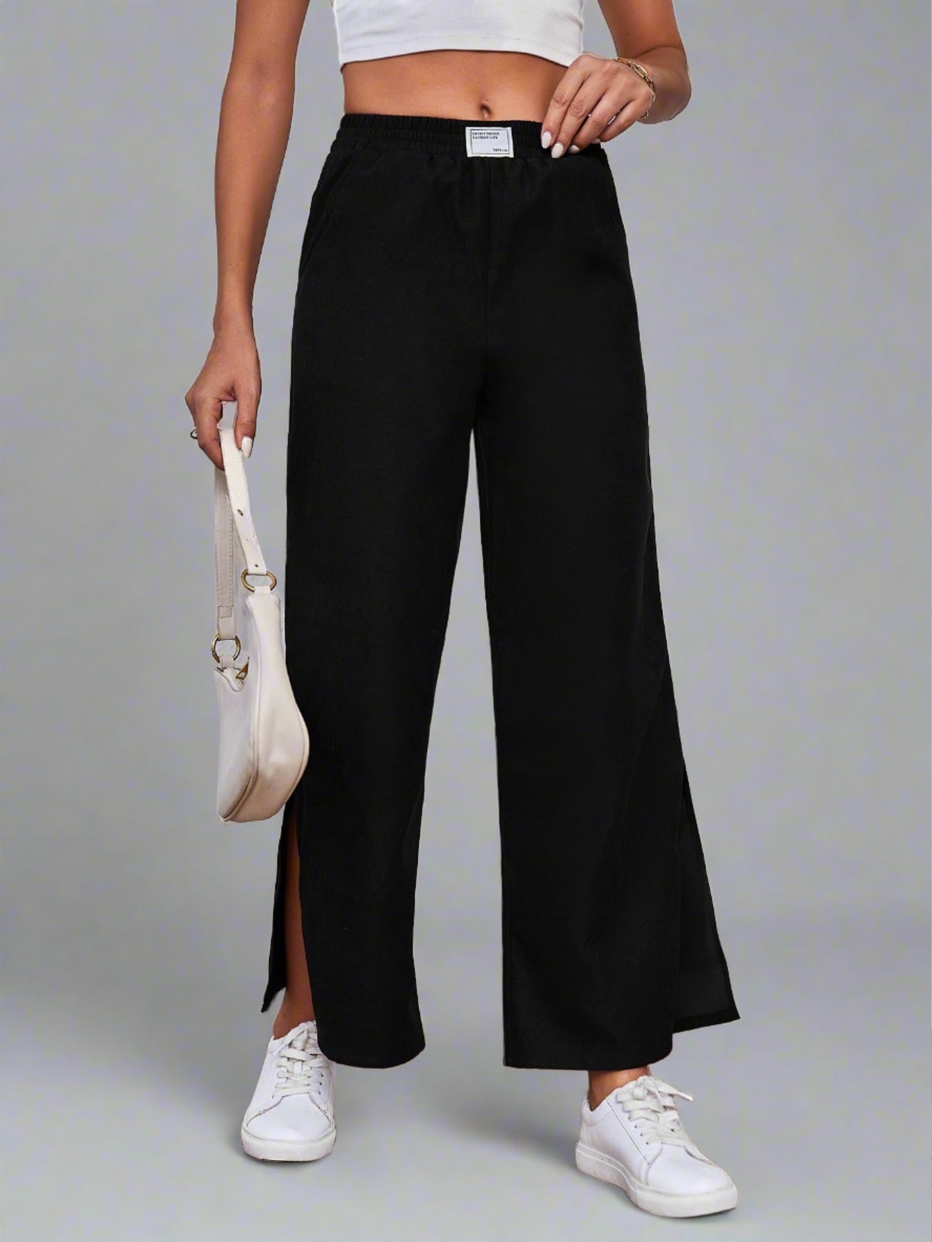 Woman wearing black wide-leg lounge pants with an elastic waistband and side slits, paired with a white crop top and sneakers.