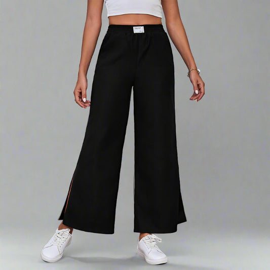 Woman wearing black wide-leg lounge pants with an elastic waistband and side slits, paired with a white crop top and sneakers.