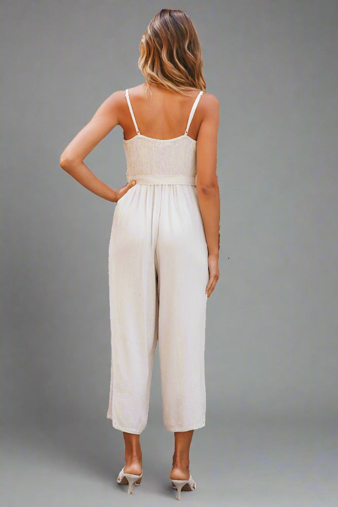 Woman wearing a beige linen jumpsuit with a V-neckline and tie belt, perfect for travel.