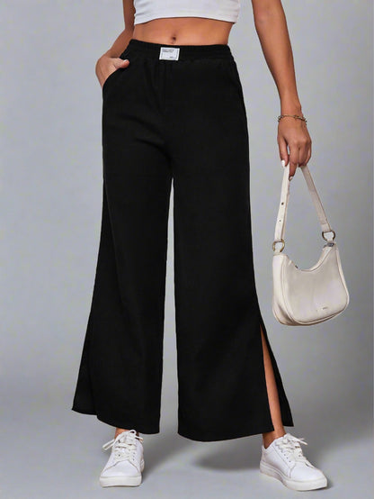 Woman wearing black wide-leg lounge pants with an elastic waistband and side slits, paired with a white crop top and sneakers.