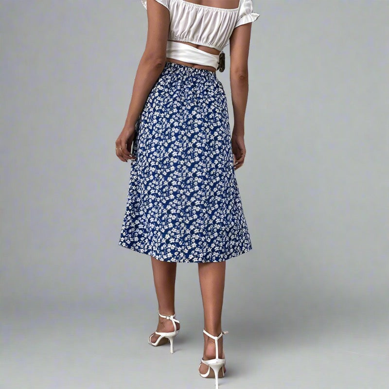 Woman wearing a blue midi skirt with a white floral print, paired with a white crop top and white strappy heels