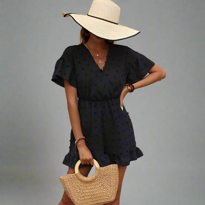 Woman wearing a black romper with polka dot texture, V-neckline, flutter sleeves, and ruffled hem, styled with a wide-brimmed hat